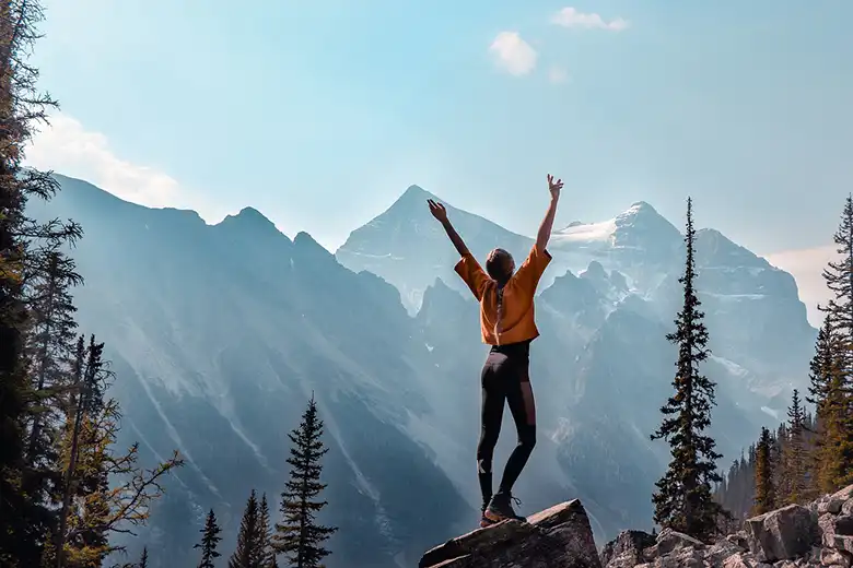 Mujer levantando los brazos rodeada de montañas