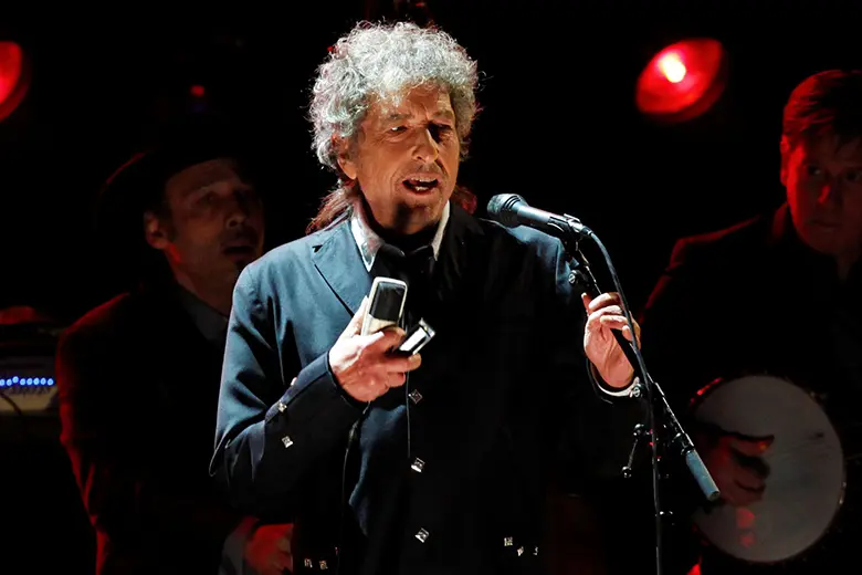 La imagen muestra a Bob Dylan sonriendo sobre un escenario.