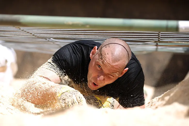 La imagen muestra a un hombre arrastrándose en el suelo durante una competencia deportiva.